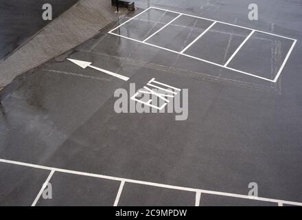 A concept image of an exit sign with an arrow taken from above on the pavement of an outside empty car park showing the exit and empty spaces. Stock Photo