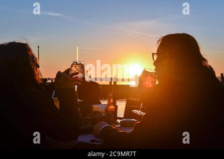 Friends drinking an aperitif in an outdoor cafe on the lakefront at sunset, Bardolino, Lake Garda, Verona, Veneto, Italy Stock Photo