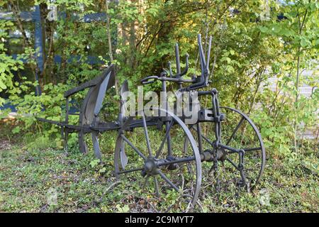 Old restored iron black farm plow exposed in the grass patch in front of secondary school in Switzerland Stock Photo