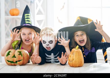 Happy brother and two sisters on Halloween. Funny kids in carnival costumes indoors. Cheerful children play with pumpkins. Stock Photo