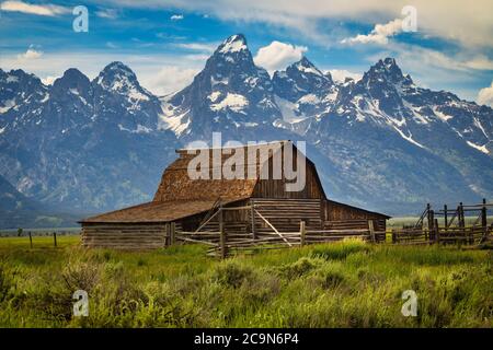 A daytime view of the Mormon Row barn below the Grand Teton Mountain Range on a cloudy day Stock Photo