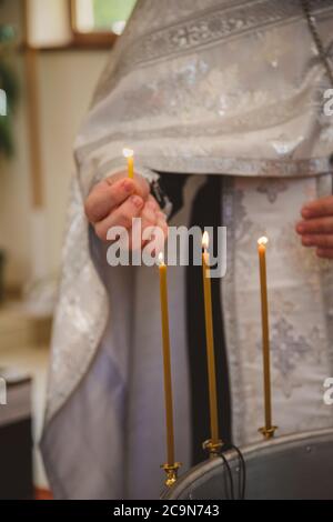 Christening in the church, priest is lighting candles at children baptismal font. Details in the orthodox christian church Stock Photo