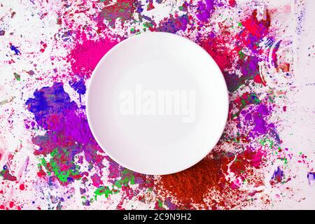 A ceramic white plate placed on a colour powder splattered background. Holi festival theme. Stock Photo