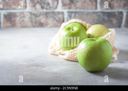Organic green apples in reusable cotton net bag on wooden table. Eco-package, zero waste concept. Selective focus. Stock Photo
