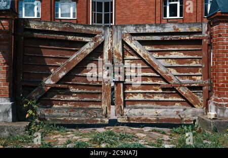 Shabby wooden gates with a lock near brick country house Stock Photo