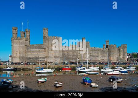 Caernarfon Castle Welsh medieval historical stone fortress building on River Seiont boats in landscape UNESCO heritage tourism Gwynedd North Wales UK Stock Photo