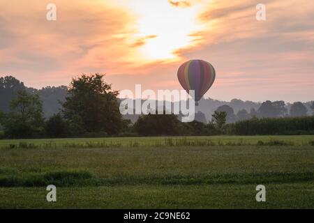 Hot Air Balloon floats over grass field and rolling hills at sunrise Stock Photo