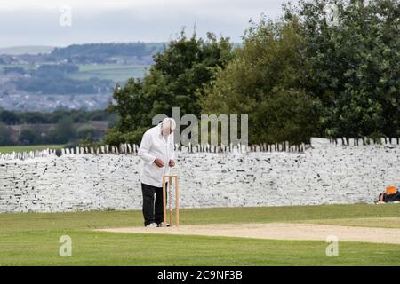 Cricket umpire behind the stumps consulting a notebook while officiating at a village cricket match in West Yorkshire on a Saturday afternoon Stock Photo