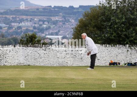 Umpire in a cricket match dressed in a traditional white coat officiating from a square leg position in a Yorkshire village cricket match Stock Photo