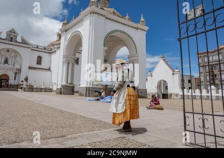 COPACABANA, BOLIVIA - JANUARY 16, 2016: A bolivian woman wearing traditional clothes walks in front of the Basilica Our lady of Copacabana, in Bolivia Stock Photo