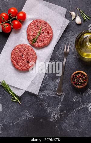 Fresh raw meat burger cutlet with herbs and spices on the black stone board, top view Stock Photo