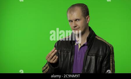 Rocker man employee asking for salary increase, smiling to camera and showing money gesture, needs more cash, financial reward, credit, loan. Portrait of guy biker posing on chroma key background Stock Photo