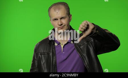 Dislike to you. Rocker man in brown leather jacket pointing to camera and showing thumbs down, looking dissatisfied upset about choice, making disapproval sign. Stock Photo