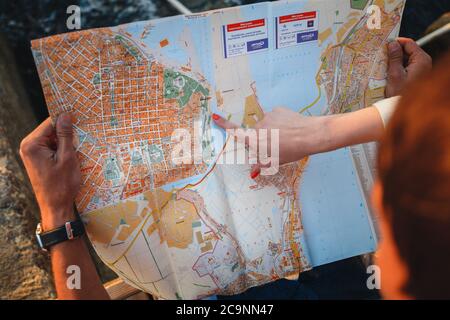 ODESSA, UKRAINE - AUGUST 06, 2015: Close up of young couple sitting on the wooden deck at port with a map in hands, pointing, travel concept Stock Photo