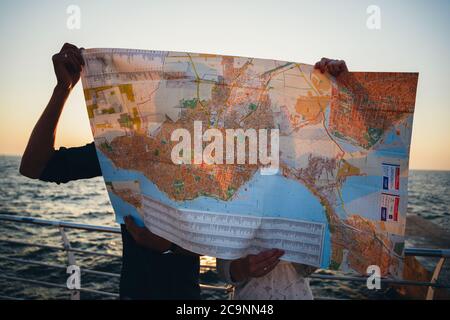 ODESSA, UKRAINE - AUGUST 06, 2015: A silhouette of young couple kissing hiding behind a printed map of the city, at port, beach with a map in hands Stock Photo