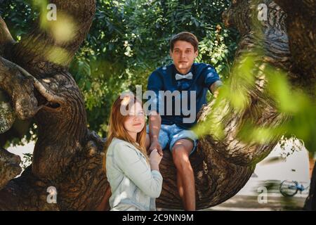 Happy stylish loving couple of hipsters hugging in a park, man sitting on a tree Stock Photo