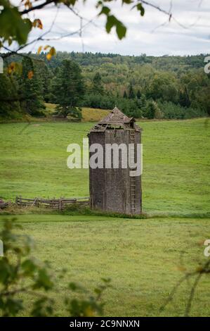 An old abandoned wooden silo in a green pasture near Ardoch Ontario. There is lush green forest in the background Stock Photo