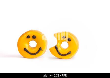 two Fresh yellow donuts with a chocolate smile, one missing bite isolated on white background with soft shadow Stock Photo