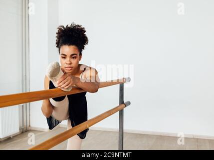 Young ballerina stretching her leg in dance studio. Woman doing