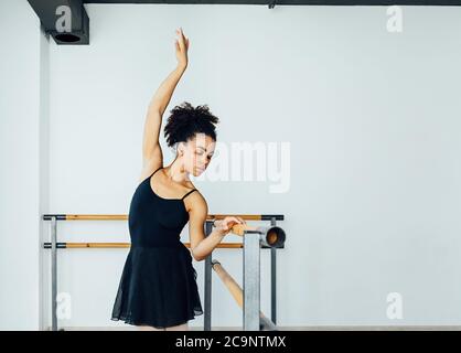 Young beautiful ballerina practicing ballet moves at barre in small studio Stock Photo