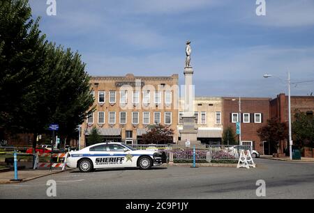 Graham, North Carolina, USA. 1st Aug, 2020. A County Sheriff sits in front of the Alamance County Courthouse. Last weekend, Barrett Brown, the president of the NAACPÃs area branch, grabbed a cardboard poster and slipped across the line of orange cones that demarcated the legal protest zone. He crossed a traffic circle and stood silently next to the Confederate monument in front of the Alamance County Courthouse. One of the 12 deputy sheriffs guarding the 30-foot-tall monument, a marble statue of a Confederate soldier atop a granite column, directed Brown to leave. When he refused, the deputy Stock Photo