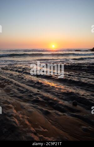 Rocks on the beach in the evening, the sun is hiding in the horizon, north of Spain Stock Photo