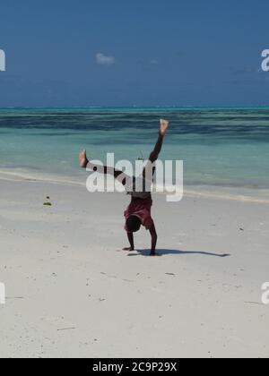 Young black boy doing handstand on white sand beach, Zanzibar,Tanzania Stock Photo