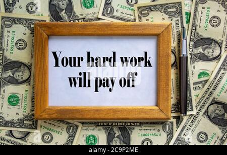 Wooden picture frame with inscription 'your hard work will pay off' on beautiful background from dollar bills and metalic pen. Concept. Stock Photo