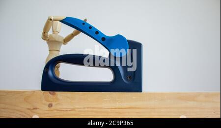 A construction stapler on a wooden bar. Wooden model of human. Beautiful white background. Copy space. Stock Photo