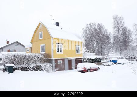 Yellow Swedish two-story single family house with a broken roof constructed in the late 1940s during snowfall in the winter season. Stock Photo