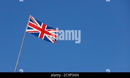 The British flag is waving on a flagpole against a clear blue sky. Stock Photo