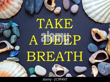 Text 'take a deep breath' on a beautiful black background. Sea stones and seashells. Concept. Stock Photo
