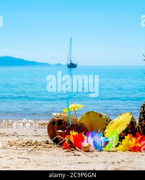 Pineapples and coconuts on the sand by the sea with a boat on the background Stock Photo