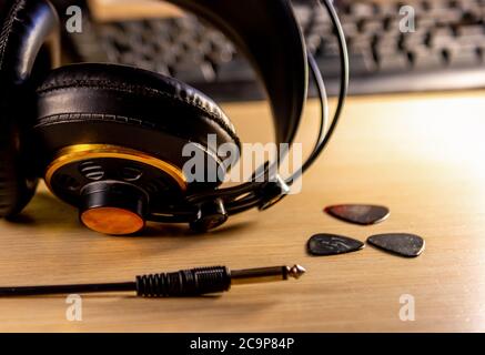 Headphones and guitar picks with a computer keyboard on the background on a wooden desk Stock Photo