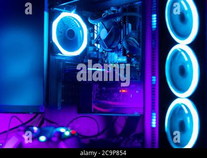 Glass pc case with rgb lighting and a desk with a game pad on the foreground Stock Photo