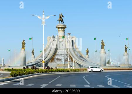 Fountain with sculptures in a roundabout in Ashgabat, Turkmenistan. Statues of Oguz Khan and his sons. Giant fountain pools structure. White car. Stock Photo