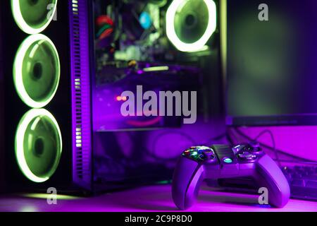 Game controller and glass pc case with rgb lighting on a wooden desk Stock Photo