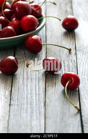 red cherries in ceramic plate on wooden table, vertical shot