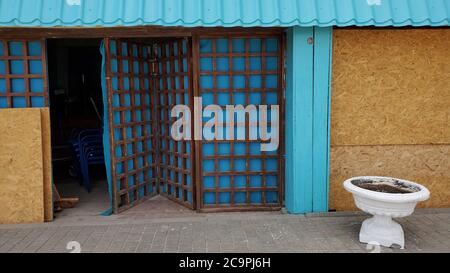 Old building exterior with opened front door and wooden lattice on blue folding screen. Retro style white stone flower bed in front of brown plywood w Stock Photo