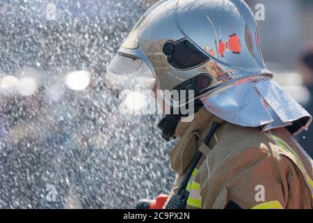 Side view of rescuer in silver mirrored helmet and protective uniform, water drops falling on firefighter Emercom of Russian Federation MChS Stock Photo