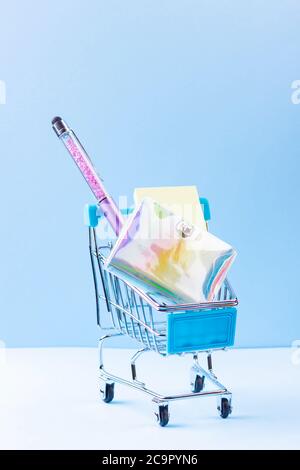 Shopping cart with school supply. School notepad with holographic cover. Stationery in shopping trolley. Back to school concept Stock Photo