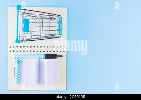 Back to school concept. Shopping cart and stationery on blue background. Pen, notepad and shopping trolley. Time to study. Top view Stock Photo