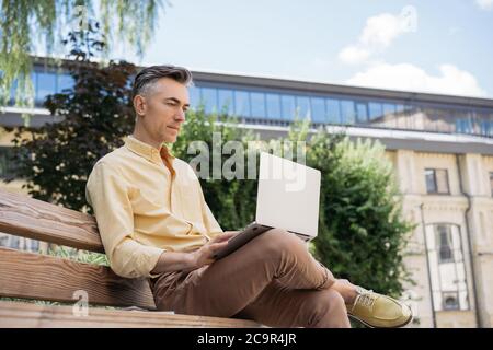 Serious mature businessman using laptop computer, planning start up, brainstorming, sitting outdoors. Busy freelancer working in park Stock Photo