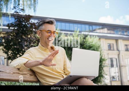 Handsome mature businessman using laptop, working project, watching training courses, sitting on bench. Smiling man having video conference Stock Photo