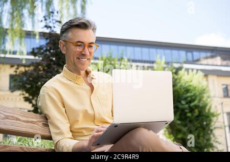 Freelancer copywriter using laptop computer, typing on keyboard. Portrait of handsome mature man having video conference Stock Photo
