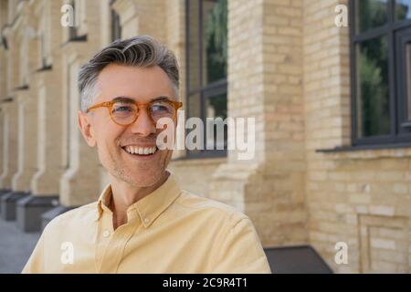 Closeup portrait of handsome mature businessman wearing stylish eyeglasses, walking on the street, laughing. Successful business concept Stock Photo