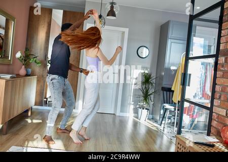 romantic funny couple dancing at home, attractive redheadyoung woman and handsome african man are enjoying spending time together Stock Photo