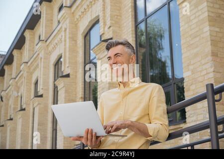 Businessman using laptop, typing on keyboard, laughing. Handsome mature man working project, planning start up Stock Photo
