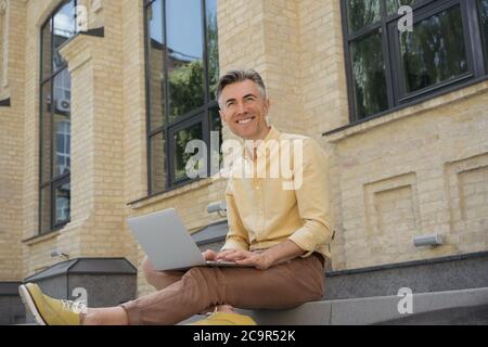 Mature businessman using laptop outdoors. Portrait of successful freelancer copywriter typing on keyboard, searching information Stock Photo