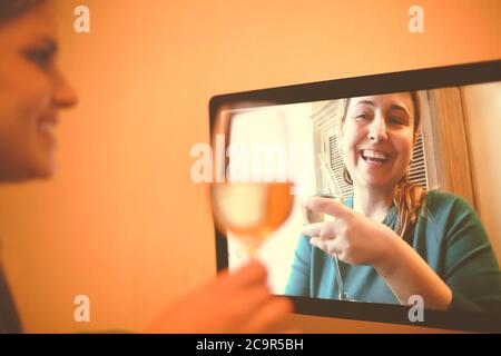 Content female friends with wineglasses communicating via video call and drinking alcohol beverages together during coronavirus epidemic